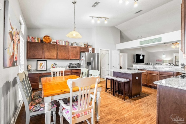 kitchen featuring stainless steel refrigerator with ice dispenser, decorative light fixtures, a breakfast bar area, and light wood-type flooring