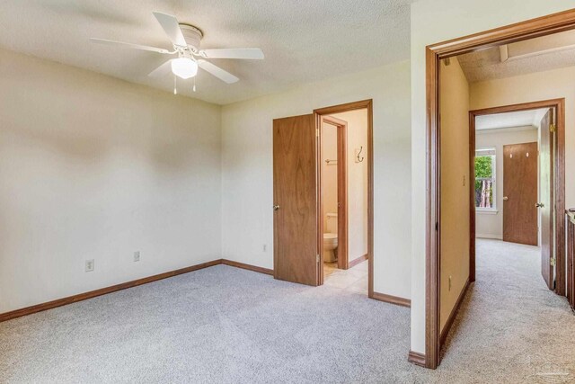 unfurnished bedroom with ensuite bathroom, a textured ceiling, ceiling fan, and light colored carpet