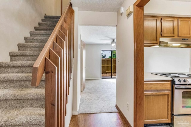 staircase with ceiling fan, wood-type flooring, and a textured ceiling