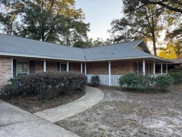 view of front of property with covered porch, a shingled roof, and brick siding