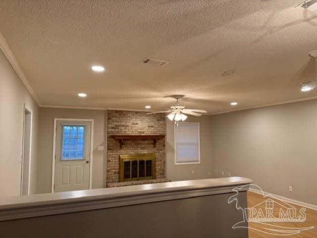 unfurnished living room featuring a textured ceiling, visible vents, a ceiling fan, ornamental molding, and a brick fireplace