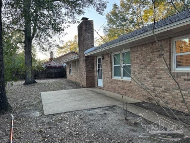 exterior space featuring brick siding, fence, a chimney, and a patio