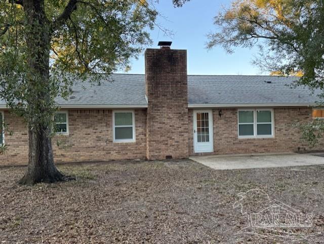 rear view of house with brick siding, roof with shingles, a chimney, and a patio