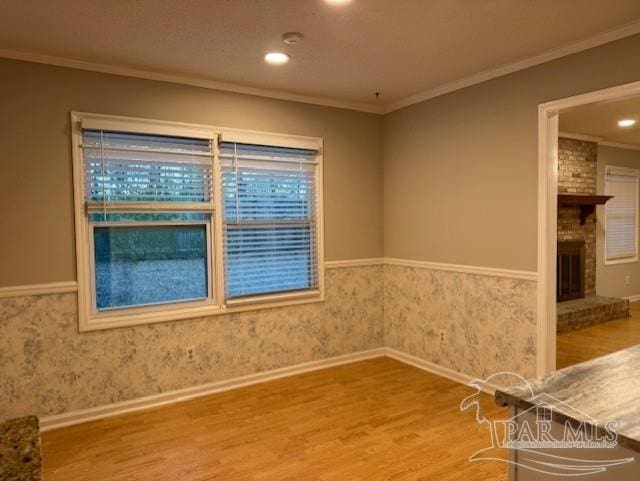 empty room featuring a wainscoted wall, a fireplace, ornamental molding, and wood finished floors