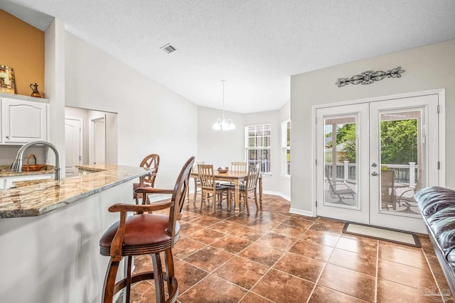 dining area featuring french doors, a textured ceiling, dark tile patterned floors, an inviting chandelier, and lofted ceiling