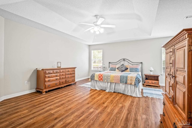 bedroom with wood-type flooring, a textured ceiling, a raised ceiling, and ceiling fan