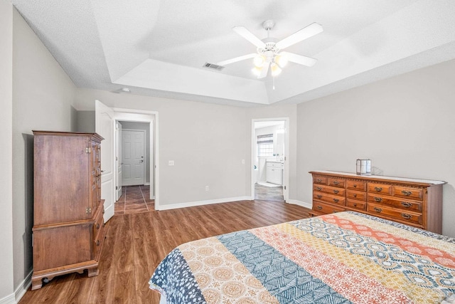 bedroom with ensuite bathroom, a raised ceiling, dark hardwood / wood-style floors, ceiling fan, and a textured ceiling