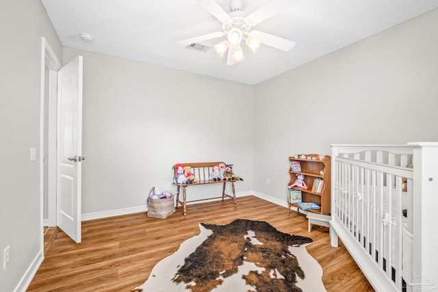 bedroom with hardwood / wood-style flooring, ceiling fan, and a nursery area