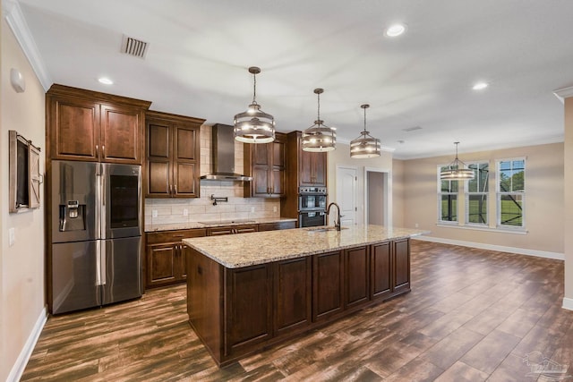 kitchen featuring stainless steel appliances, hanging light fixtures, a kitchen island with sink, and wall chimney exhaust hood