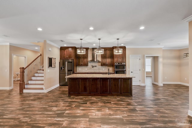 kitchen featuring wall chimney exhaust hood, sink, stainless steel fridge with ice dispenser, pendant lighting, and a kitchen island with sink