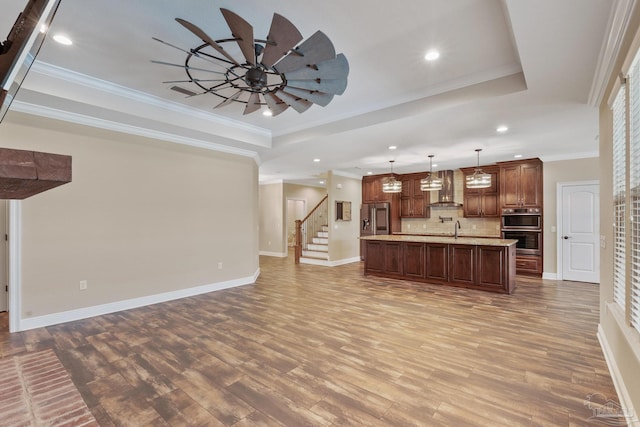 kitchen featuring a tray ceiling, decorative light fixtures, stainless steel fridge, and wall chimney exhaust hood