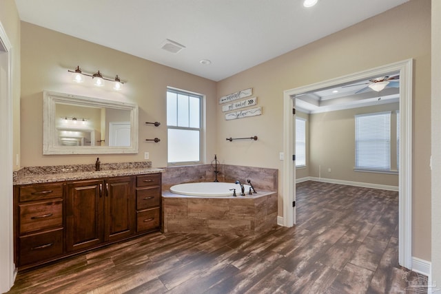 bathroom featuring hardwood / wood-style flooring, vanity, ornamental molding, a relaxing tiled tub, and a raised ceiling