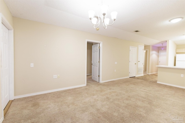 unfurnished room with a textured ceiling, light carpet, and a notable chandelier