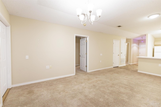 empty room featuring light colored carpet, a textured ceiling, and a chandelier