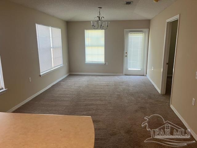 unfurnished dining area featuring a textured ceiling, carpet flooring, and a notable chandelier