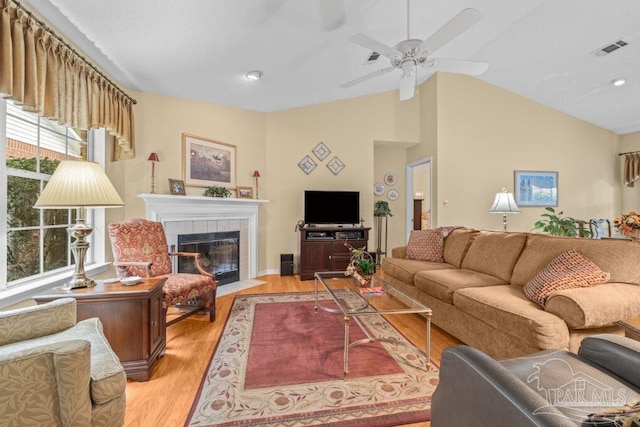 living room featuring vaulted ceiling, ceiling fan, a fireplace, and light hardwood / wood-style floors