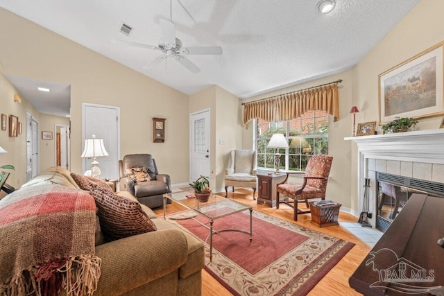 living room with lofted ceiling, light hardwood / wood-style flooring, ceiling fan, a textured ceiling, and a tiled fireplace