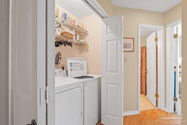 clothes washing area featuring separate washer and dryer, a textured ceiling, and light hardwood / wood-style flooring