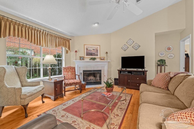 living room featuring vaulted ceiling, a fireplace, light wood-type flooring, ceiling fan, and a textured ceiling