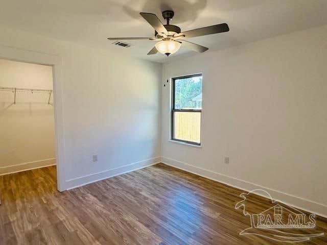 unfurnished bedroom featuring ceiling fan, a closet, a spacious closet, and dark hardwood / wood-style floors