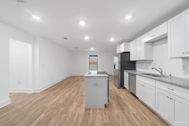 kitchen with light stone countertops, stainless steel appliances, sink, white cabinetry, and a kitchen island