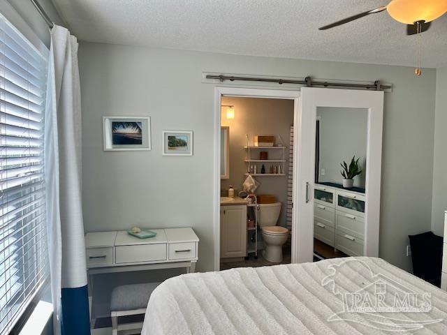 bedroom with ensuite bathroom, a barn door, a textured ceiling, and multiple windows