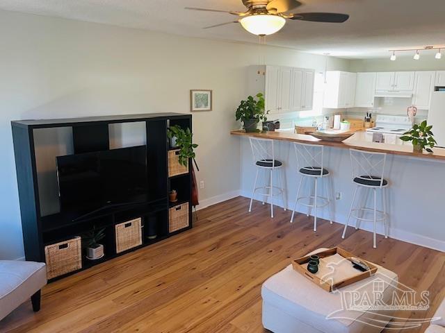 kitchen featuring white cabinets, ceiling fan, light wood-style floors, white appliances, and a kitchen breakfast bar