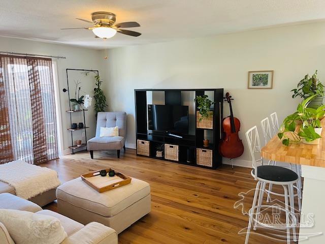 living area with baseboards, a ceiling fan, and wood finished floors