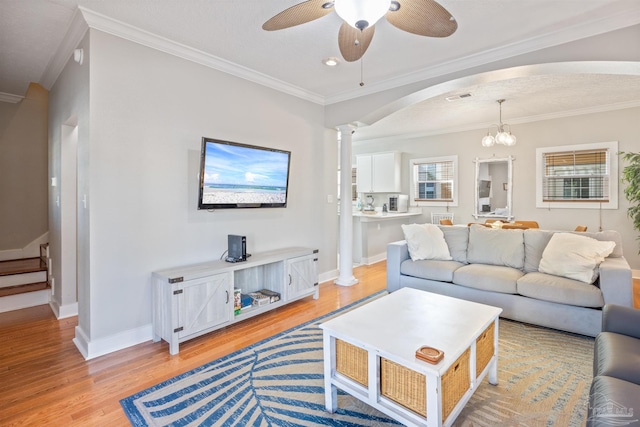 living room with ceiling fan with notable chandelier, ornamental molding, decorative columns, and light hardwood / wood-style floors