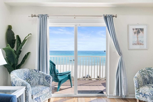 interior space with a water view, light wood-type flooring, baseboards, and a view of the beach