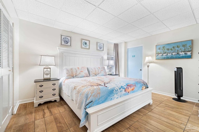 bedroom with wood finished floors, a paneled ceiling, and baseboards