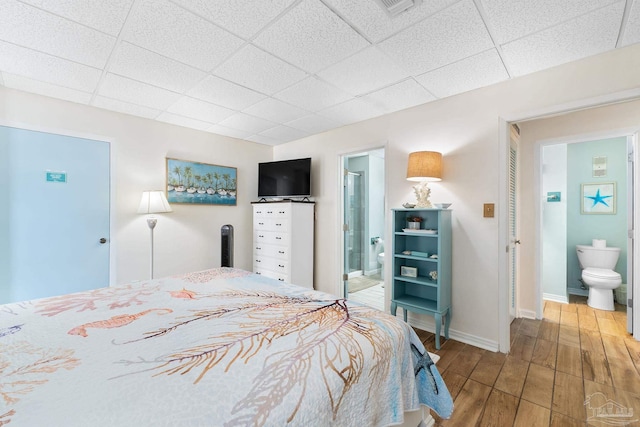 bedroom with baseboards, a drop ceiling, wood finished floors, and ensuite bathroom