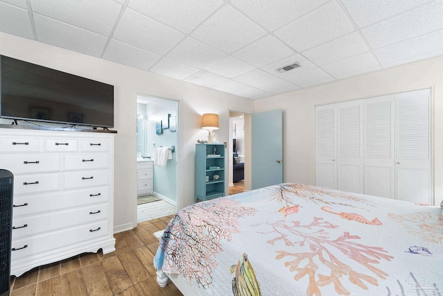 bedroom featuring dark wood finished floors, a paneled ceiling, a closet, visible vents, and connected bathroom