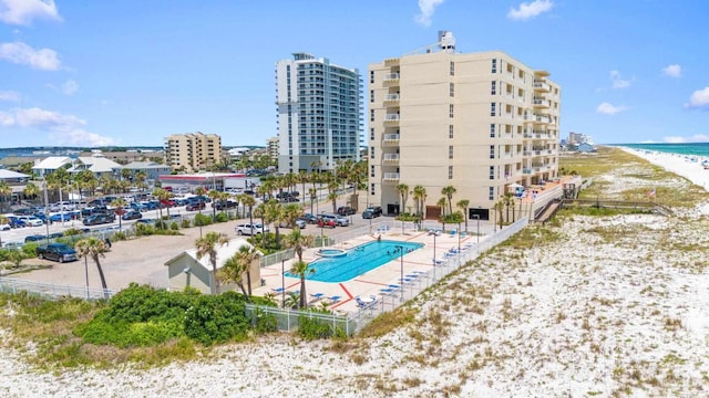 pool with a city view, a view of the beach, a water view, a patio area, and fence