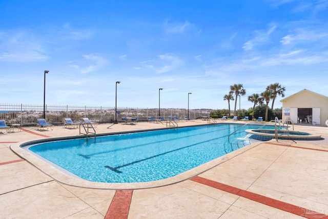 community pool with a hot tub, fence, and a patio