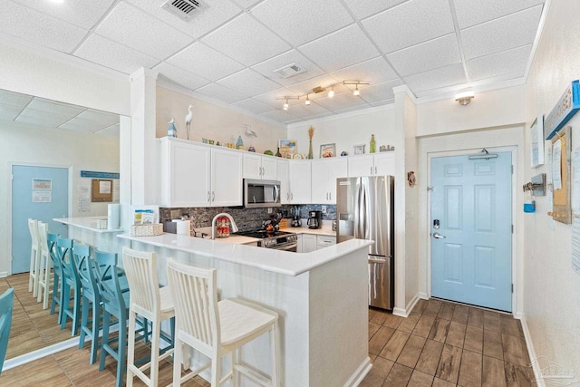 kitchen featuring light countertops, backsplash, appliances with stainless steel finishes, white cabinetry, and a peninsula