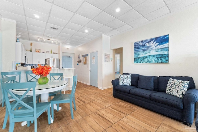 living area featuring a drop ceiling, visible vents, baseboards, ornamental molding, and light wood finished floors