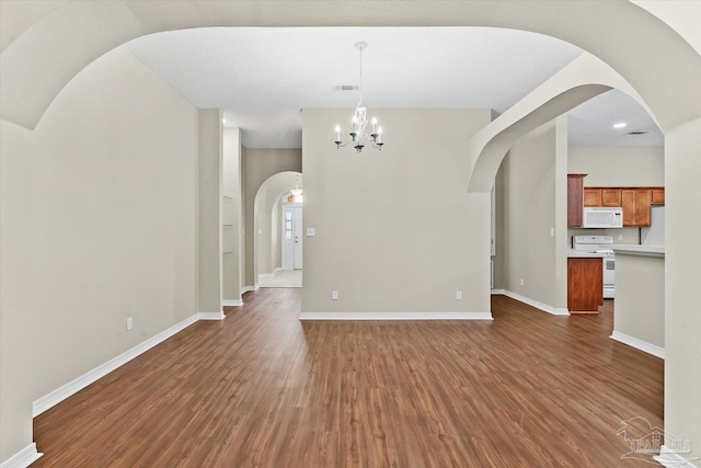 unfurnished living room featuring an inviting chandelier and dark wood-type flooring