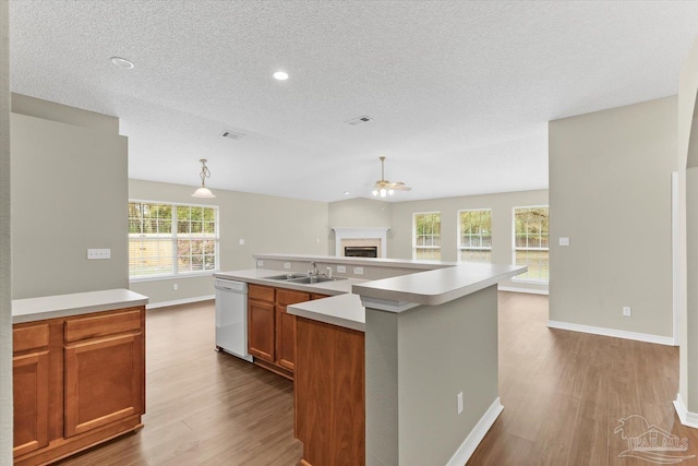 kitchen featuring sink, decorative light fixtures, a center island with sink, light wood-type flooring, and white dishwasher