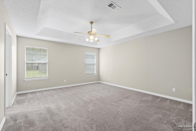 carpeted empty room with a raised ceiling, ceiling fan, and a textured ceiling