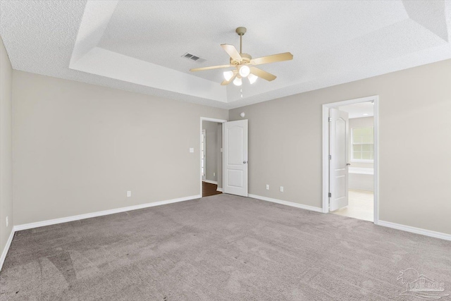 unfurnished bedroom with ensuite bathroom, a textured ceiling, a raised ceiling, carpet floors, and ceiling fan