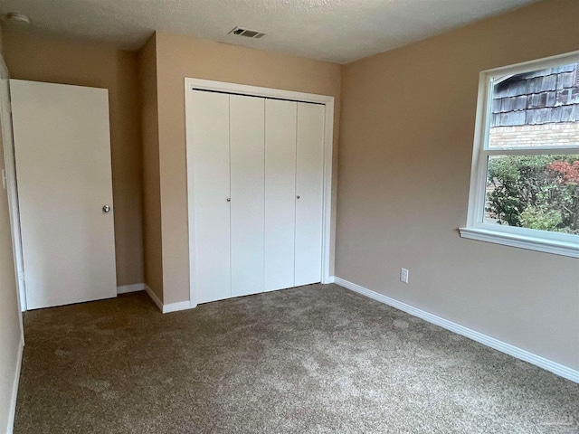 unfurnished bedroom featuring dark colored carpet, a textured ceiling, and a closet