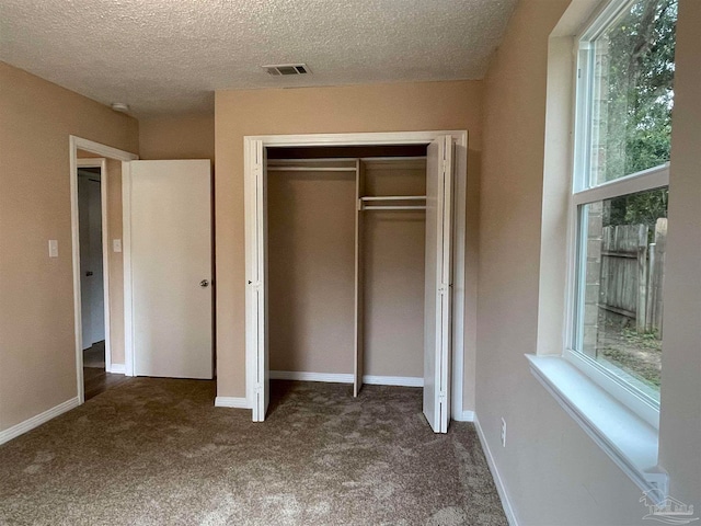 unfurnished bedroom featuring dark colored carpet, a textured ceiling, and a closet