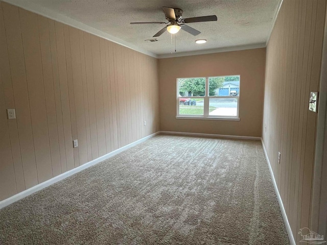 spare room with ceiling fan, wooden walls, light colored carpet, and a textured ceiling