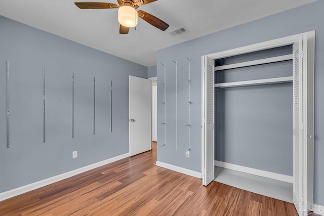 unfurnished bedroom featuring baseboards, visible vents, ceiling fan, wood finished floors, and a closet