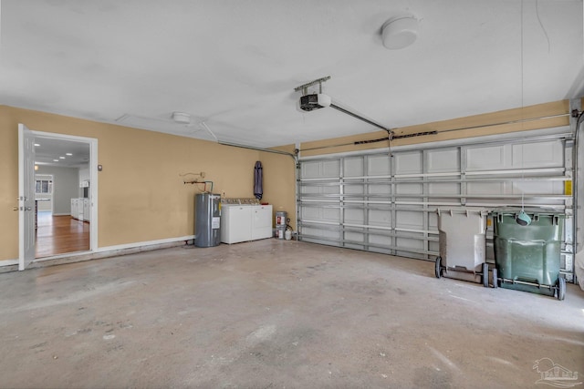 garage featuring washing machine and dryer, baseboards, a garage door opener, and electric water heater