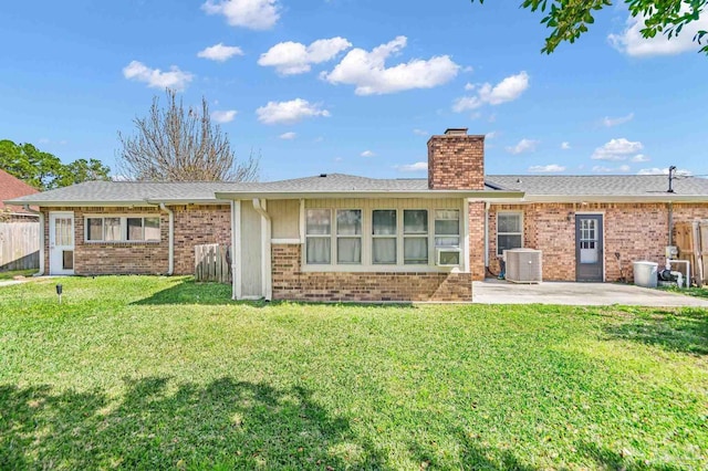 rear view of property with brick siding, fence, a lawn, a chimney, and a patio area