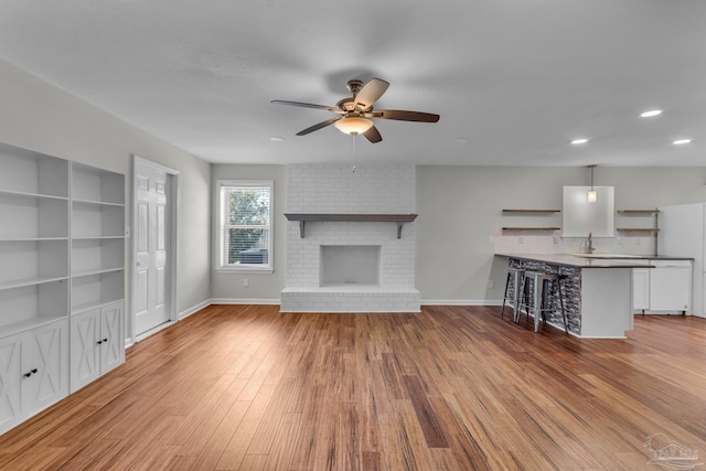 unfurnished living room featuring ceiling fan, a sink, wood finished floors, baseboards, and a brick fireplace