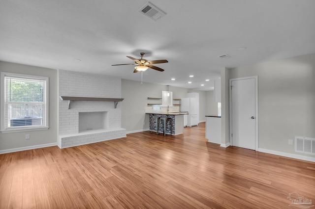 unfurnished living room with light wood-style floors, ceiling fan, a fireplace, and visible vents