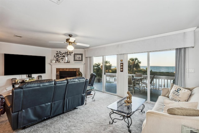 living room with a tile fireplace, ceiling fan, light colored carpet, a water view, and ornamental molding